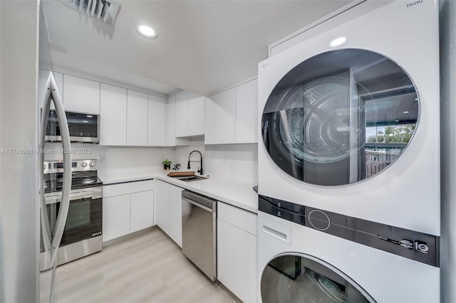 kitchen with stacked washer and dryer, sink, white cabinets, and stainless steel appliances