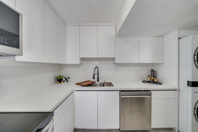 kitchen with sink, stainless steel appliances, stacked washer and clothes dryer, and white cabinets