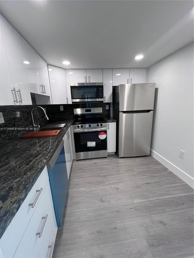 kitchen featuring sink, dark stone countertops, white cabinets, stainless steel appliances, and light wood-type flooring