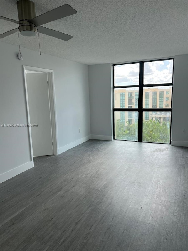 empty room with ceiling fan, a wall of windows, dark hardwood / wood-style floors, and a textured ceiling