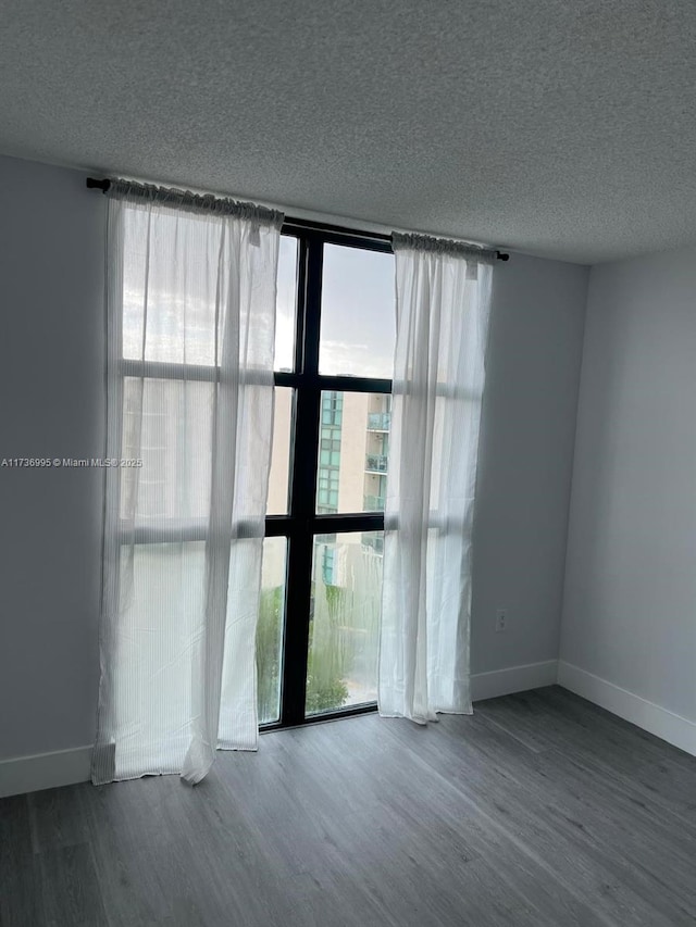 empty room with hardwood / wood-style floors, a wealth of natural light, a textured ceiling, and a wall of windows