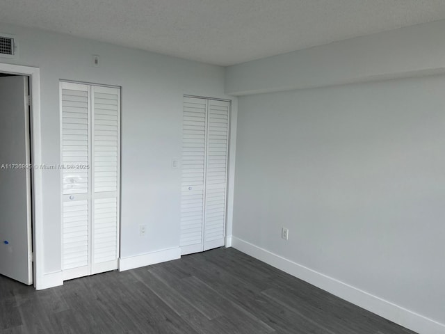 unfurnished bedroom featuring multiple closets, dark hardwood / wood-style floors, and a textured ceiling