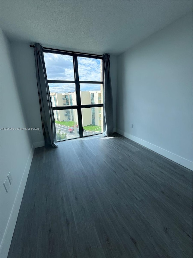 empty room with dark hardwood / wood-style floors, a textured ceiling, and a wall of windows