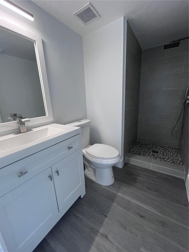 bathroom featuring a tile shower, vanity, wood-type flooring, and toilet