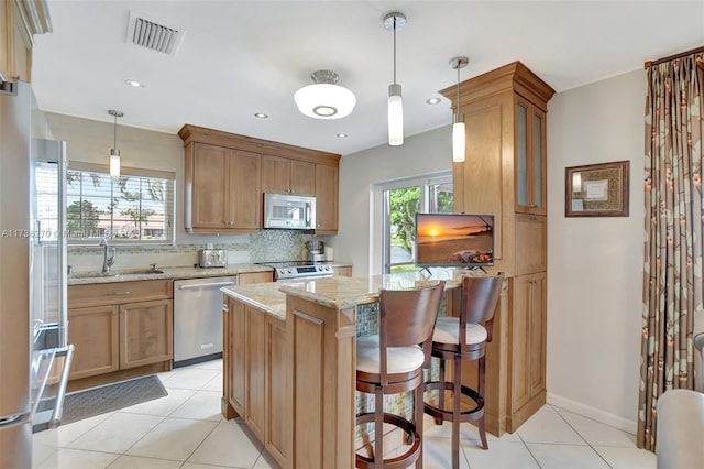 kitchen with sink, decorative light fixtures, a center island, stainless steel appliances, and light stone countertops