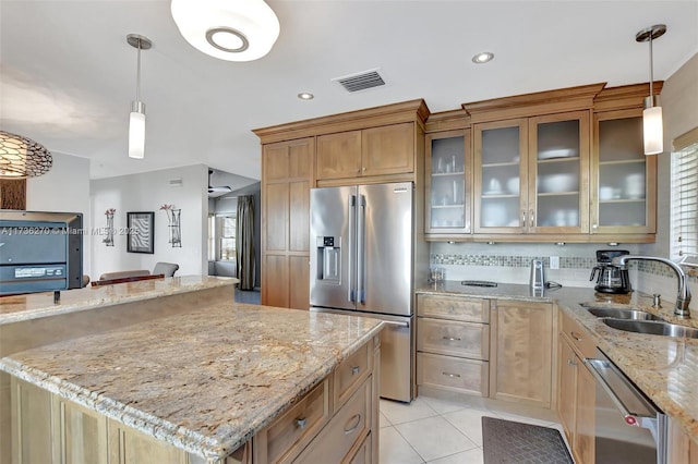 kitchen with sink, light stone counters, appliances with stainless steel finishes, a kitchen island, and pendant lighting