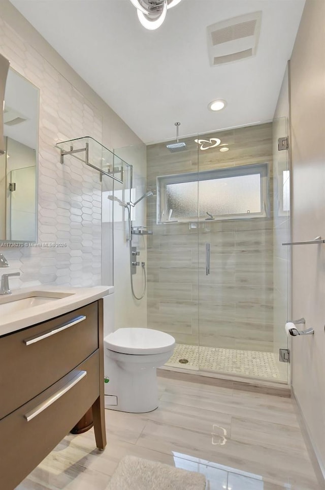 bathroom with tile walls, vanity, decorative backsplash, a shower with shower door, and toilet