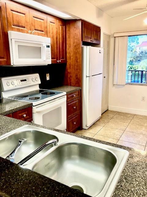 kitchen featuring ceiling fan, light tile patterned floors, white appliances, and dark stone counters