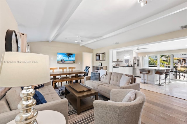 living room featuring vaulted ceiling with beams, ceiling fan, and light wood-type flooring