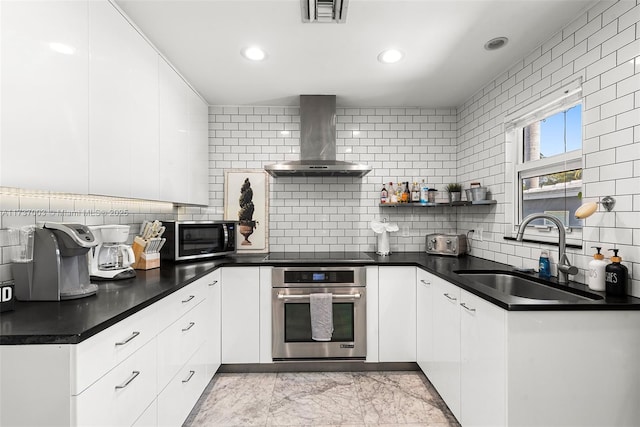 kitchen with wall chimney exhaust hood, appliances with stainless steel finishes, sink, and white cabinets