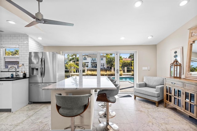 kitchen with sink, white cabinetry, light stone counters, tasteful backsplash, and stainless steel fridge with ice dispenser