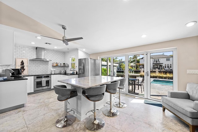 kitchen with appliances with stainless steel finishes, tasteful backsplash, white cabinetry, lofted ceiling, and wall chimney exhaust hood