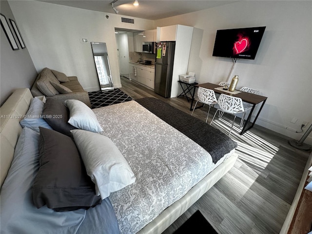 bedroom with dark hardwood / wood-style flooring, rail lighting, and black fridge