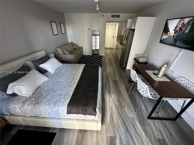 bedroom with stainless steel fridge and dark hardwood / wood-style flooring