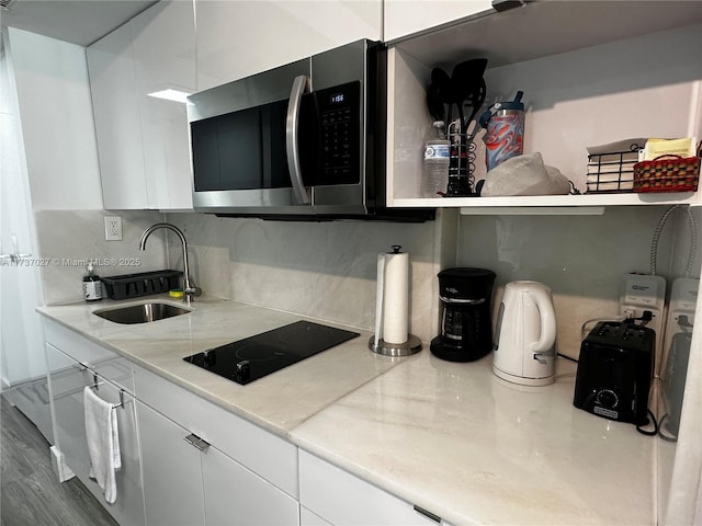 kitchen featuring white cabinetry, wood-type flooring, sink, backsplash, and black electric stovetop