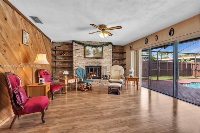 sitting room featuring ceiling fan, a fireplace, wood-type flooring, and wooden walls