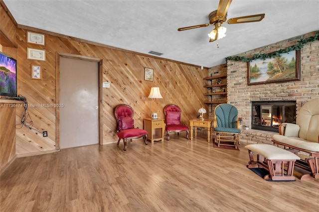 sitting room with a brick fireplace, hardwood / wood-style flooring, wooden walls, and ceiling fan