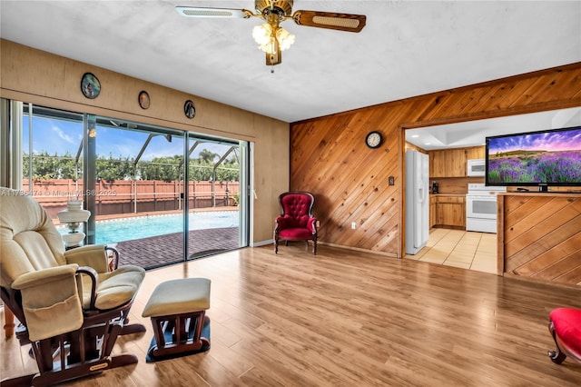 living area featuring ceiling fan, light hardwood / wood-style floors, and wood walls