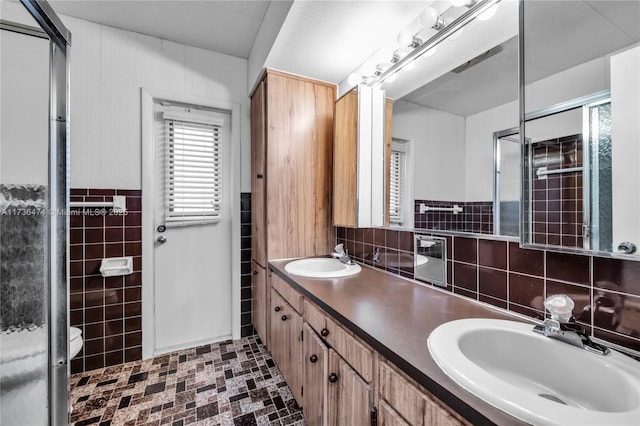 bathroom with vanity, toilet, an enclosed shower, and tile walls