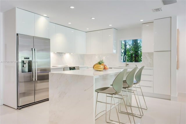 kitchen featuring sink, a breakfast bar, tasteful backsplash, white cabinets, and stainless steel fridge with ice dispenser