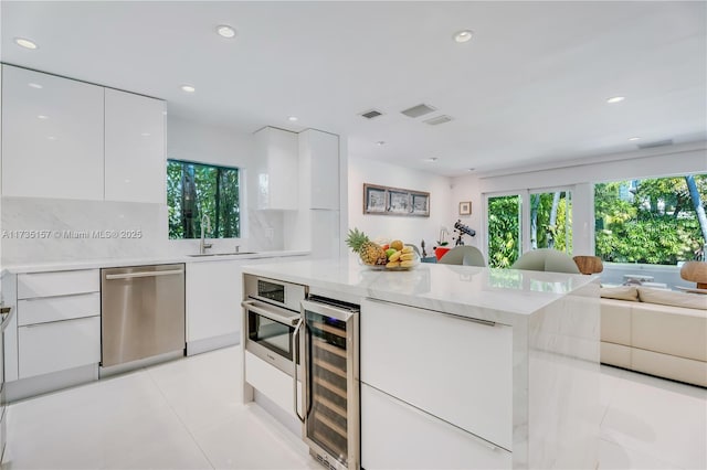 kitchen with sink, light tile patterned floors, appliances with stainless steel finishes, beverage cooler, and white cabinets