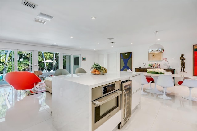 kitchen with a kitchen island, pendant lighting, oven, wine cooler, and white cabinets