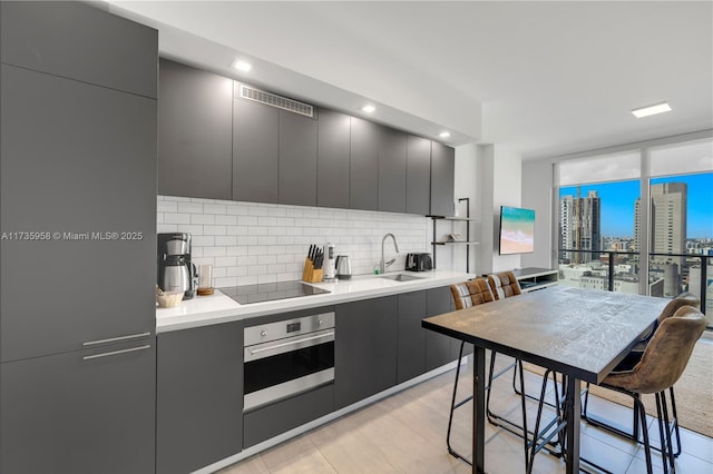 kitchen with sink, oven, a wall of windows, decorative backsplash, and black electric stovetop