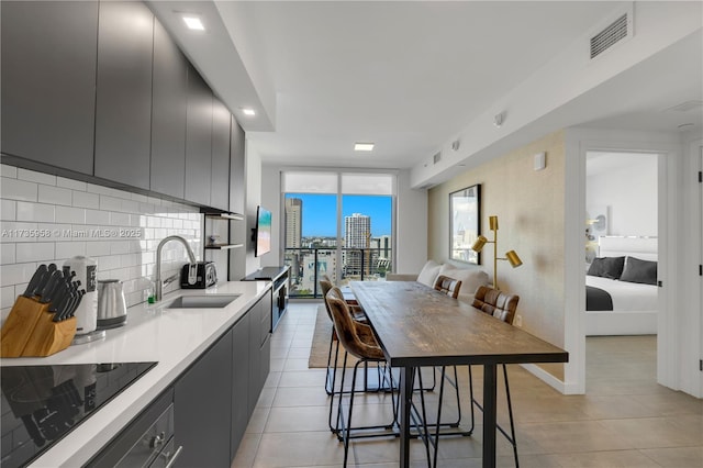 kitchen featuring sink, light tile patterned floors, expansive windows, black electric cooktop, and decorative backsplash