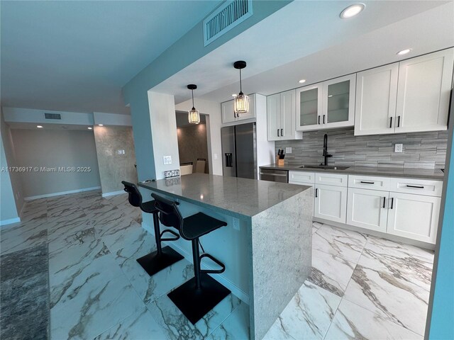 kitchen featuring a kitchen bar, sink, white cabinetry, hanging light fixtures, and appliances with stainless steel finishes