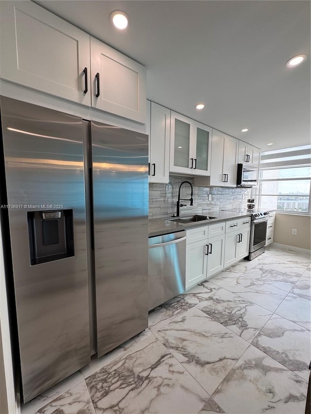 kitchen featuring marble finish floor, stainless steel appliances, backsplash, white cabinetry, and a sink