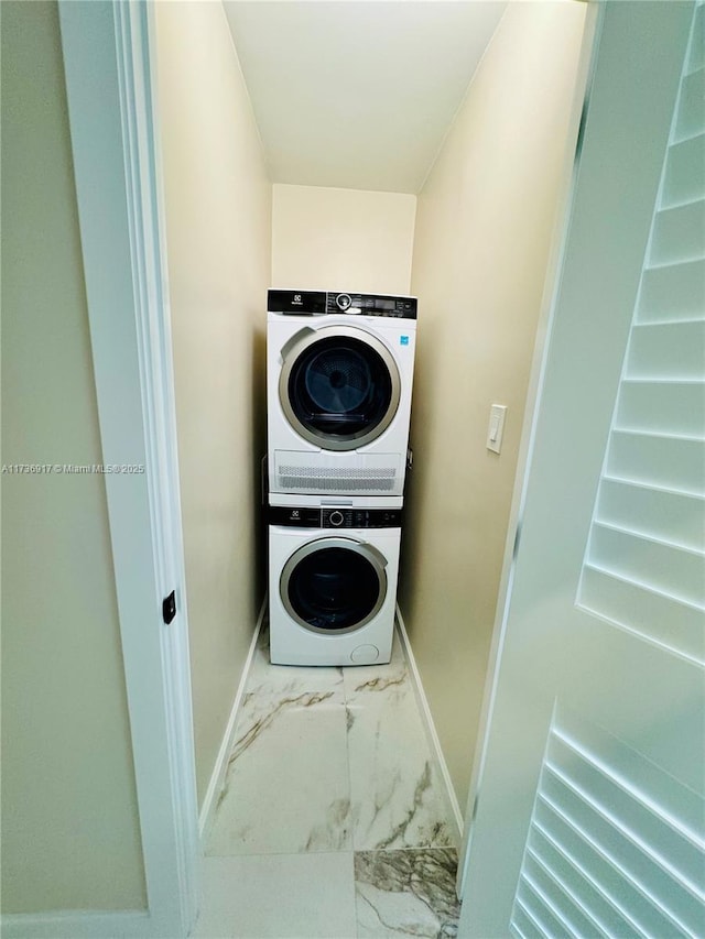 laundry area featuring marble finish floor, baseboards, stacked washing maching and dryer, and laundry area