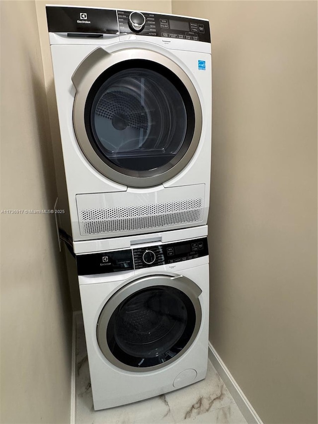 clothes washing area with marble finish floor, baseboards, laundry area, and stacked washer and clothes dryer