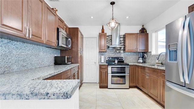 kitchen featuring light stone countertops, pendant lighting, appliances with stainless steel finishes, wall chimney exhaust hood, and a sink