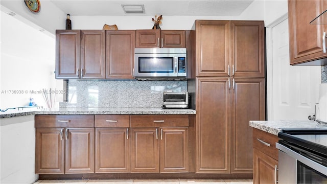 kitchen featuring visible vents, stainless steel microwave, tasteful backsplash, a toaster, and light stone countertops