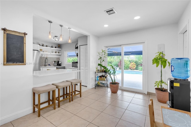 kitchen with light tile patterned floors, white cabinetry, hanging light fixtures, a kitchen breakfast bar, and tasteful backsplash