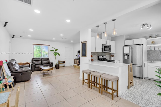 kitchen with appliances with stainless steel finishes, a kitchen breakfast bar, kitchen peninsula, pendant lighting, and white cabinets