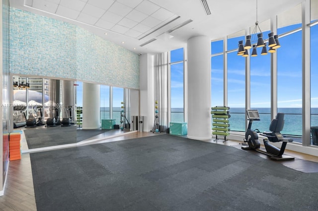 gym featuring a water view, an inviting chandelier, wood-type flooring, expansive windows, and a towering ceiling