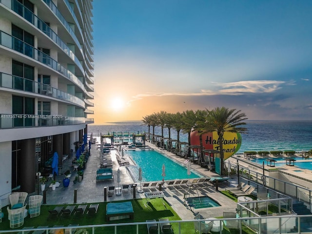 pool at dusk with a water view and a patio