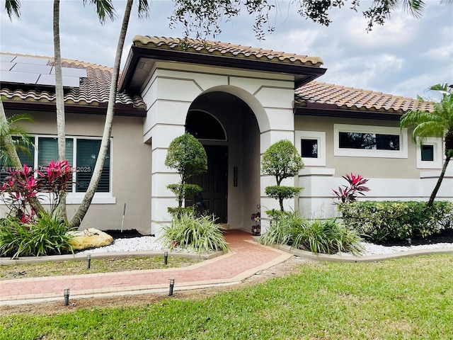 view of front facade featuring a front yard, a tiled roof, roof mounted solar panels, and stucco siding