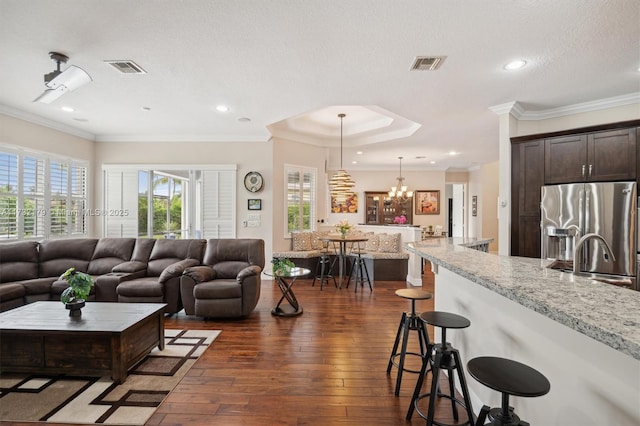 living room with a textured ceiling, dark wood-style flooring, visible vents, and crown molding