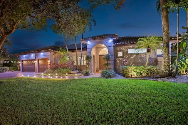 mediterranean / spanish house featuring a garage, driveway, a tile roof, a yard, and stucco siding