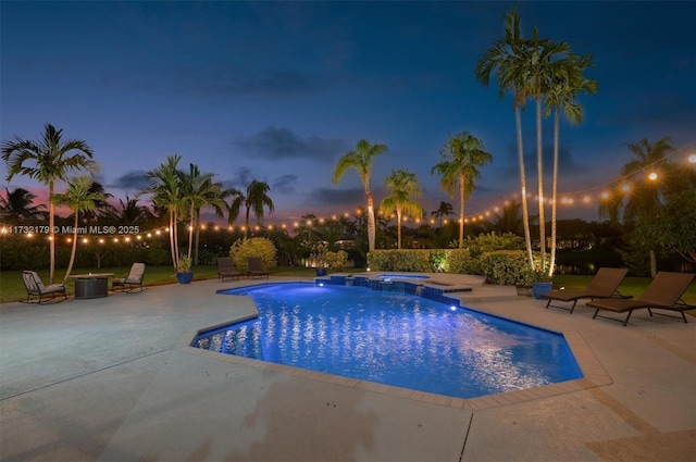 pool at dusk with a pool with connected hot tub and a patio area