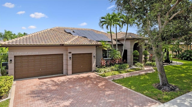 mediterranean / spanish-style home featuring a garage, decorative driveway, roof mounted solar panels, a front lawn, and stucco siding