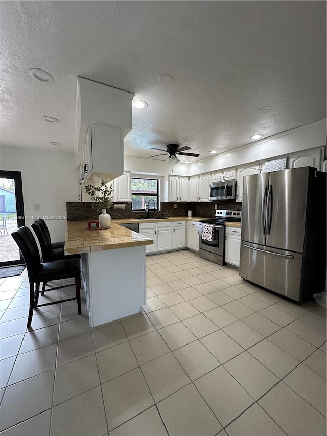 kitchen featuring sink, appliances with stainless steel finishes, tile counters, kitchen peninsula, and white cabinets