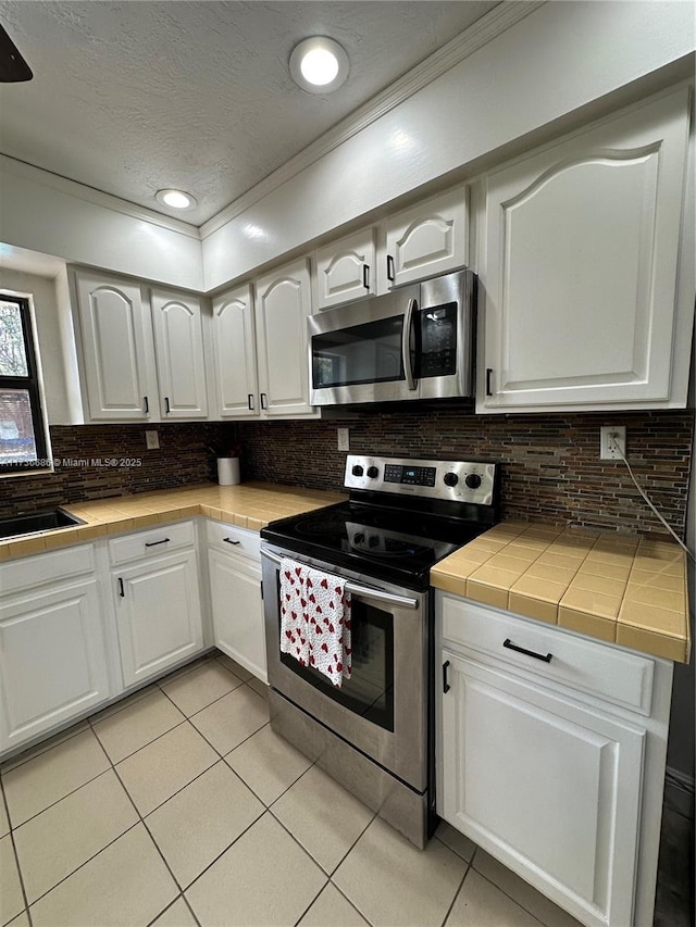 kitchen featuring stainless steel appliances, tile counters, white cabinets, and decorative backsplash