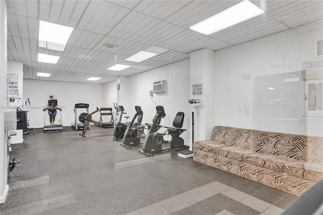 exercise room with an AC wall unit and a paneled ceiling