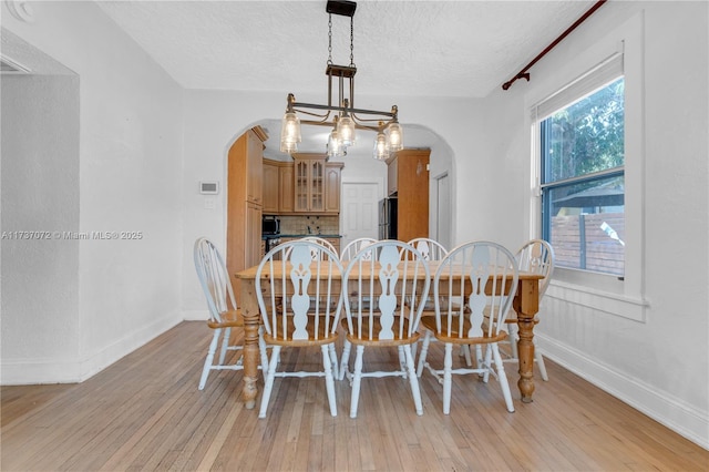 dining room with arched walkways, light wood-type flooring, a textured ceiling, and baseboards