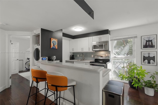 kitchen with a breakfast bar, sink, kitchen peninsula, stainless steel appliances, and white cabinets