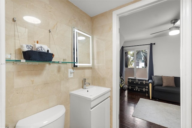 bathroom featuring hardwood / wood-style floors, tile walls, vanity, ceiling fan, and toilet