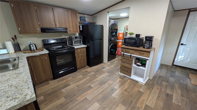 kitchen featuring sink, crown molding, dark hardwood / wood-style floors, stacked washing maching and dryer, and black appliances